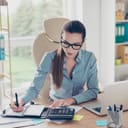 Woman using a calculator and taking down notes in an office