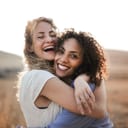 Close-up of two women joyfully hugging outdoors, celebrating their friendship.