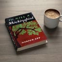 To Kill a Mockingbird book and a coffee mug on a wooden table