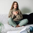 young woman practicing pranayama in a lotus position on a bed, trying to reduce stress or anxiety levels
