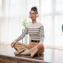 portrait of a young woman using headphones for guided meditation, seated on the floor of her living room with eyes closed