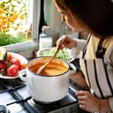 A woman making pumpkin soup in a large pot on a gas stove