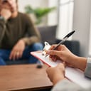 young man undergoing a psychology session with a female therapist at a clinic, close-up on her hands writing something down