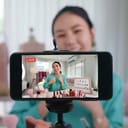 Woman recording herself on smartphone in front of a selection of beauty products