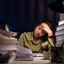 tired young woman working late at her desk surrounded by books and papers