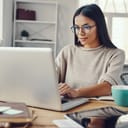 A beautiful young woman in casual clothing smiling while using a laptop indoors.