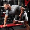 side view of a bodybuilder performing dumbbell rows on a bench, focusing on back muscles in a gym