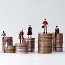 Artistic depiction of wealth inequality: Miniature people standing on piles of different heights of coins