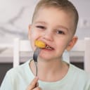 Close-up of a joyful child enjoying chicken nuggets at home.