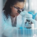 portrait of a young female scientist examining a sample under a microscope in a medical science laboratory