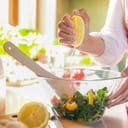 Close-up of a woman's hands drizzling fresh lemon juice over a bowl of salad.