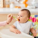 Close-up of a woman feeding a baby, while the baby is seated in a baby feeder.