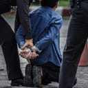 Man on his knees being handcuffed by a police officer with another officer standing close behind them