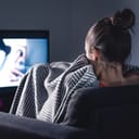 A woman watching a scary movie hiding behind a blanket