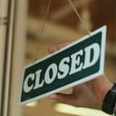 close-up view of a young man's hands flipping a "close" sign in the door of his cafe