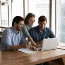 A business team of three discussing something, while looking at the laptop screen in the office.