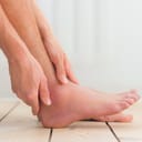 close-up of a person holding their swollen ankle with hands