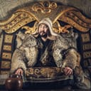 A person portraying Genghis Khan sitting at a throne wearing ceremonial tunic and a fur coat