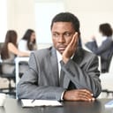 A businessman in a suit sitting alone away from his colleagues with a pensive expression on his face