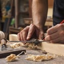 hand of a carpenter taking measurement of a wooden plank
