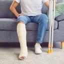 A man with a broken leg sits on the sofa in the living room.