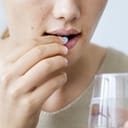 A woman taking a pill with a glass of water