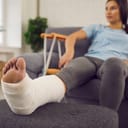 A woman sitting in a sofa with a broken leg and crutches beside her