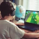 A closeup of a young boy with headphones playing video games on a laptop