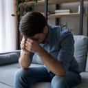 depressed young man sitting on a sofa with his head down on his hands