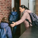 woman helping children with backpacks leave a building