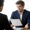 businessman dissatisfied with the paper he's reading, expressing disagreement while sitting across from his partner during the meeting