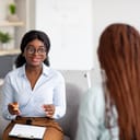 A young woman with a clipboard talking with another woman at an office