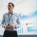 Close-up of a businessman presenting accomplishments and goals in front of a large digital screen displaying graphs and charts.