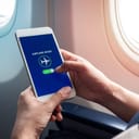 Flight mode concept. Hand holding white smartphone and turned on airplane mode on screen near the window on the airplane.