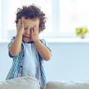 baby boy crying and rubbing his eyes while standing on the couch at home