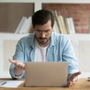 frustrated man working on a laptop in an office, looking at the laptop in front of him