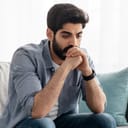 Close-up of a young upset man sitting on a sofa, deep in thought over personal struggles.