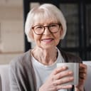 A senior woman with glasses holding a coffee mug