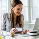 A young woman holding a credit card making a purchase online using a laptop