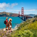 Two people standing next to the Golden Gate Bridge on a sunny day