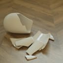 close-up of shattered pieces of a white ceramic vase on a wooden floor