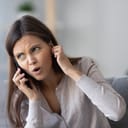 Annoyed young woman talking on the phone not hearing bad signal lost no mobile connection on cellphone, irritated girl closing ear frustrated by communication telecommunication service problem indoor
