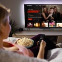 woman at home wrapped in a cozy blanket, enjoying TV shows through a streaming service while snacking on popcorn