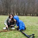 Two young children, acting as treasure hunters, using a metal detector and digging into the soil.
