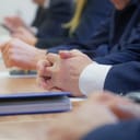 Folded hands of a politician or businessman on a table next to a notepad