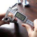 Person using a caliper to measure the diameter of a pipe