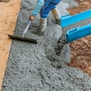 A machine pouring cement as a worker tries to level it.