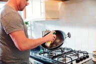 Man spraying cooking spray onto a pan in front of a stove in kitchen