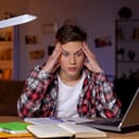 Worried young man sitting at table holding his head