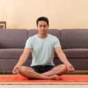 young man meditating on a mat in his living room in front of the couch